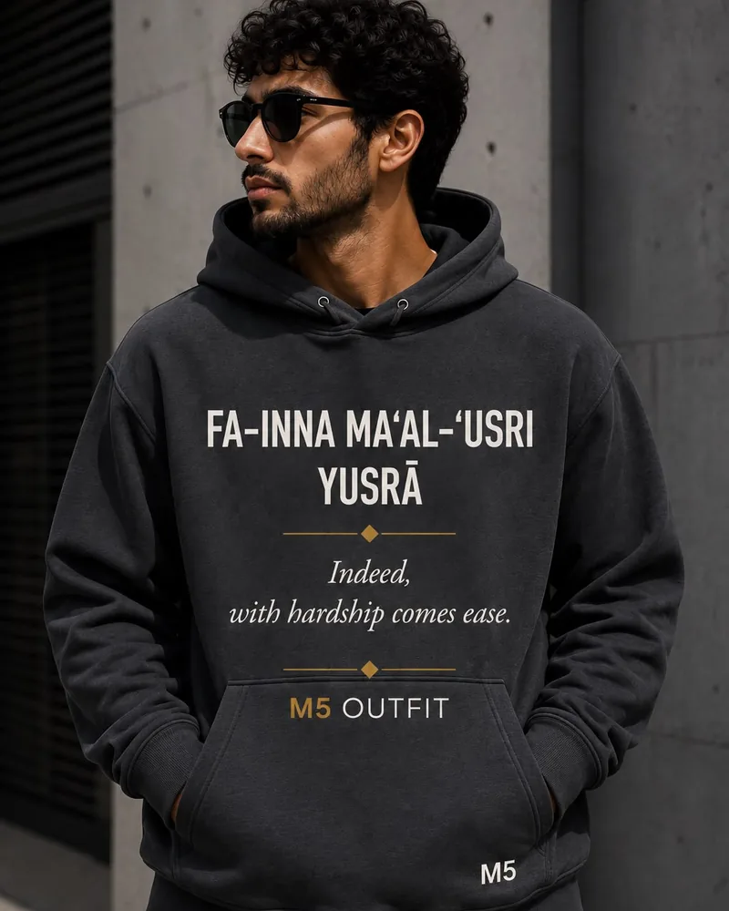 Model wearing a charcoal M5 Outfit hoodie printed with the Arabic and English phrase Fa-inna Ma'al-'Usri Yusra