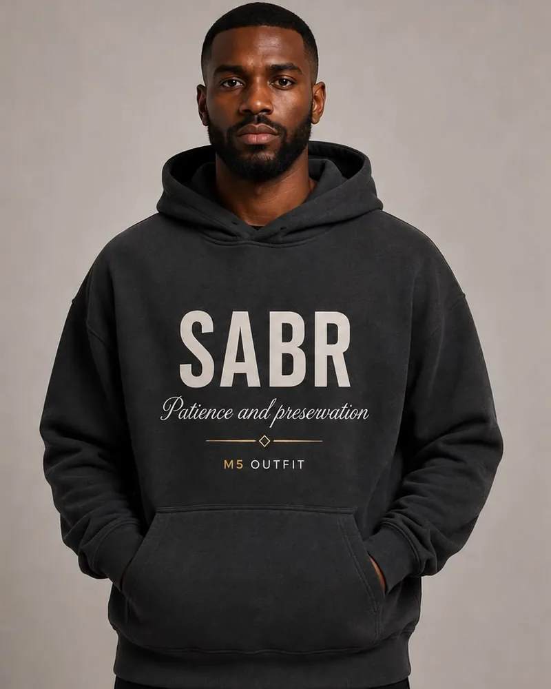 Model wearing a charcoal M5 Outfit hoodie printed with the Arabic and English word Sabr